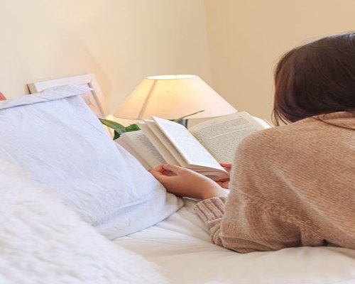 Person reading a book in bed with a warm reading lamp